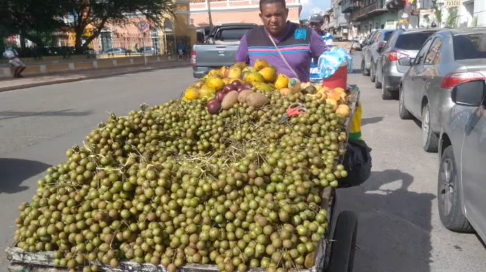a street vendor pushes his car loaded with columbian fruit